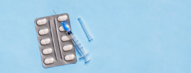 Syringe with pills in blister pack on blue background. Medicine and health care banner, poster with copy space.