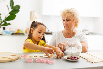 Cute little girl and her grandmother cooking on kitchen.