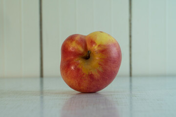 Closeup misshapen red apple with yellow spot lie on the light rustic table. Village fruit is good for eat because it contains many vitamins and microelements. Landscape orientation photo, copy space.