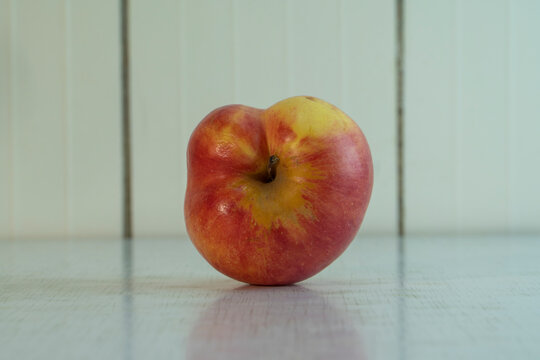 Closeup Misshapen Red Apple With Yellow Spot Lie On The Light Rustic Table. Village Fruit Is Good For Eat Because It Contains Many Vitamins And Microelements. Landscape Orientation Photo, Copy Space.