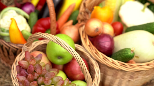 Summer fruits and vegetables in baskets. Abstract blurred image with apples, grapes, cauliflower, carrots, eggplant, peppers, onions, cucumbers, corn and zucchini in wicker baskets. Close-up shot.