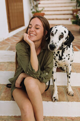 Long hair, freckled young girl sitting on a step in a green blouse playing with her Dalmatian dog