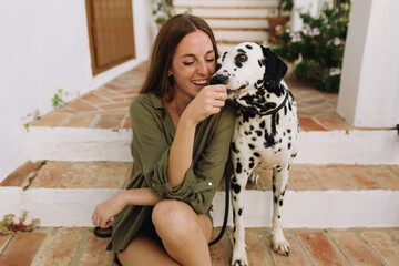 woman laughing sitting on a step and playing with her Dalmatian dog 
