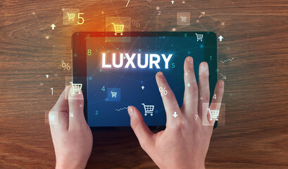 Close-up of a hand holding tablet with LUXURY inscription, online shopping concept