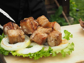 the cook removes pieces of pork skewer from the brisket on lettuce leaves and toasted onions. grilled dishes.