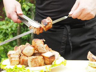 the cook removes pieces of pork skewer from the brisket on lettuce leaves and toasted onions. grilled dishes.