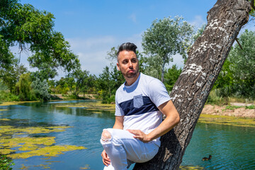 Young man in white pants and modern styling posing in the freshwater pond of Clot De La Mare De Deu...