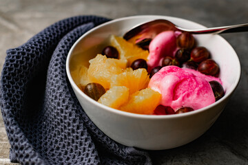 Summer refreshing dessert with fruit and berries. Pink ice cream in a bowl with orange pulp and gooseberry berries.