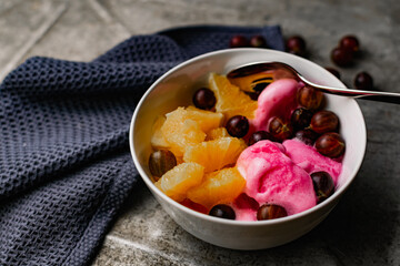 Summer refreshing dessert with fruit and berries. Pink ice cream in a bowl with orange pulp and gooseberry berries.