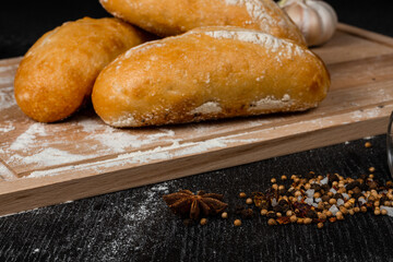 fresh white bread on a cutting board with seasonings  sprinkled with flour on a black wooden table