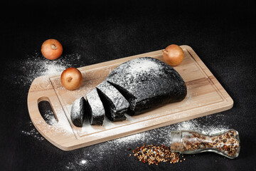 fresh black rye bread on a cutting board with flour on a black wooden table