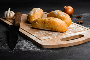 fresh white bread on a cutting board with seasonings  sprinkled with flour on a black wooden table