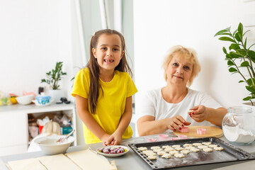 Cute little girl and her grandmother make cookies on kitchen.