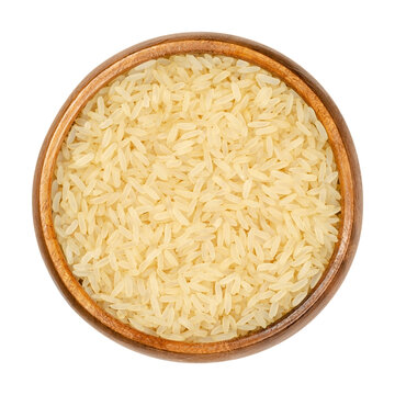 Parboiled long grain rice in wooden bowl. Converted rice, also called easy-cook rice, partially boiled in the husk through soaking, steaming and drying. Closeup, over white, isolated macro food photo.