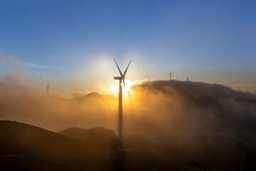 High in the mountains are wind turbines at sunrise and sunset and a sea of clouds