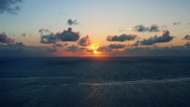 Beautiful aerial drone time-lapse of a serene ocean sunrise at Well Beach near Joao Pessoa on a warm summer morning with the water below and golden clouds on the skyline.
