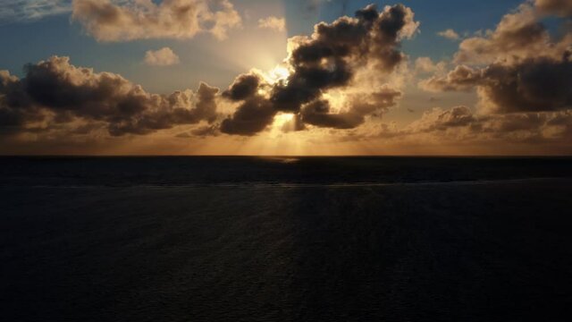 Beautiful aerial left trucking drone shot of an ocean sunrise at Well Beach near Joao Pessoa on a warm summer morning with the water below, golden clouds on the skyline, and small boats in the water.