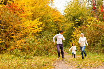 Naklejka na ściany i meble Picture of lovely family in autumn park, young parents with nice adorable daughter playing outdoors, have fun on backyard in fall, happy family enjoy autumnal nature
