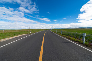 Fototapeta premium A straight asphalt road under the blue sky and white clouds