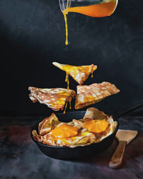 Crepes with Orange Sauce in black pan, dark background. Levitation food photography. Traditional French crepe Suzette with fresh orange sauce. Copy space. Conceptual food image.