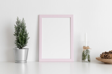 Pink frame mockup with a cypress tree, candles and pine cones on a white table. Christmas decoration.