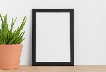 Black frame mockup with a aloe vera in a ceramic pot on a wooden table. Portrait orientation.