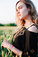 Naklejka premium Young, slender girl embroidered dress in a large wheat field at sunset