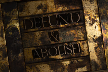 Defund and Abolish text formed with real authentic typeset letters on vintage textured silver grunge copper and gold background