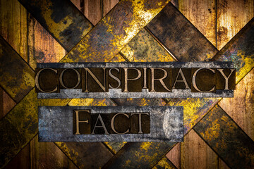 Conspiracy Fact text formed with real authentic typeset letters on vintage textured silver grunge copper and gold background