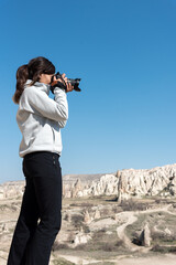 Side view of photographer woman taking shot of hills in sunny day in Cappadocia, Turkey.