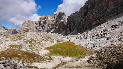 Summer landscape of Italy Dolomites. Gray mountains with natural shadows, and islets of fresh green vegetation in the valley