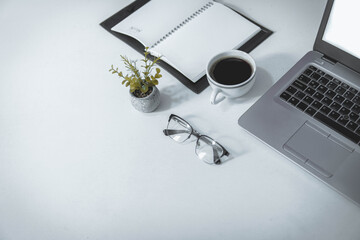 Lugar de trabajo, oficina, computadora portátil, cuaderno abierto, lentes, café y una planta, sobre un escritorio blanco, vista superior