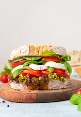 Big tasty sandwich of ciabatta with mozzarella cheese, tomatoes, basil and lettuce on the table. Sandwich with cheese and vegetables on a light background, copy space. Free space for text. 