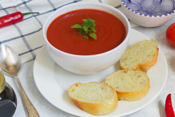 Summer diet cold gazpacho soup, tomatoes, peppers, cucumbers and greens on a white background. Sliced bread for snacks. Ice for cooling.