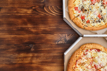 Carbonara and Hawaiian pizza in carton packs on a wooden background with copy space
