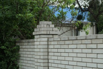 part of a white brick wall of a fence in green vegetation on a rural street