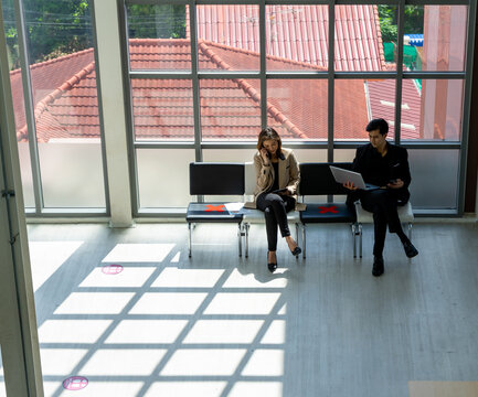 Business People Sit In The Office Far Apart From Colleague In The Office To Prevent Corona Virus Pandemic. Social Distancing New Normal Concept.