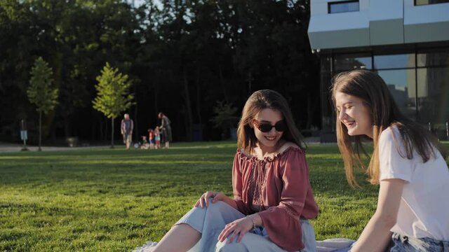Two girlfriends sitting in the park with a laptop and having fun. Viewing a webinar on entering college.
