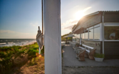 Knoten an einem Fahnenmasten vor einem weißen Haus am Strand der Südküste der dänischen Insel Bornholm bei Sonnenuntergang im Sommer.