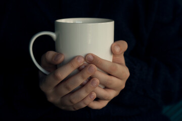Hand holding a white ceramic cup on a dark background
