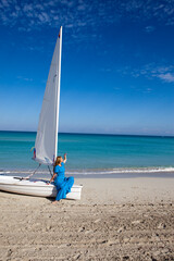 Fototapeta premium Cuba. Beautiful woman on the blue sea near the boat with a sail