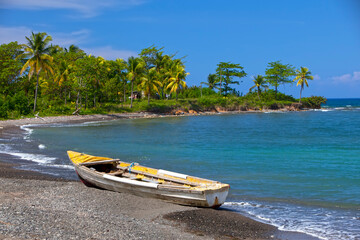 traditional wooden fishing boat on sandy sea coast with palm tree. Jamaica