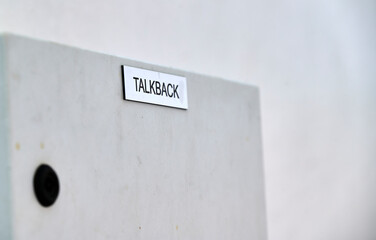 Silbernes Schild mit schwarzen Buchstaben dem Begriff "Talkback" auf einem grauen Hintergrund