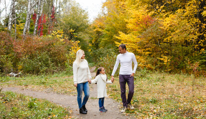Fototapeta premium Picture of lovely family in autumn park, young parents with nice adorable daughter playing outdoors, have fun on backyard in fall, happy family enjoy autumnal nature
