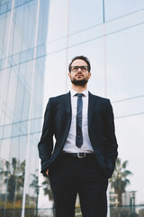 Half length portrait of a young businessman standing with his hands in the pockets near office skyscraper