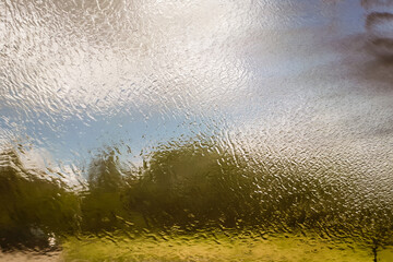 Water on glass with outdoor scenery background. Abstract rain drop on window. Surface level.