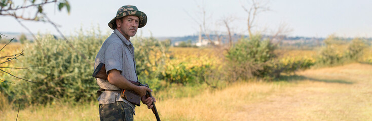 Silhouette of a hunter with a gun in the reeds against the sun, an ambush for ducks with dogs