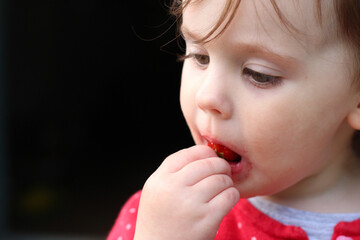 Beautiful little child with wide blond eyes and a smeared mouth eats strawberries