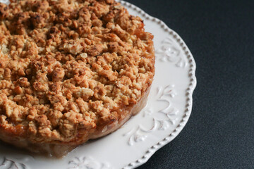 Crispy gluten free apple pie on a beautiful white plate with decoration on a dark table. Close up. Pie, apple, white plate. Autumn concept.