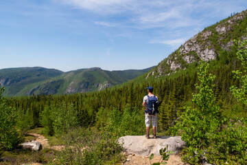 Fototapeta premium Les Grands-Jardins national park, Canada - june 2020 : back view of a hiker admiring the landscape